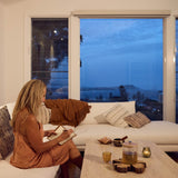 SANA wellness lifestyle – woman journaling in a cosy living room with tea ritual at sunset