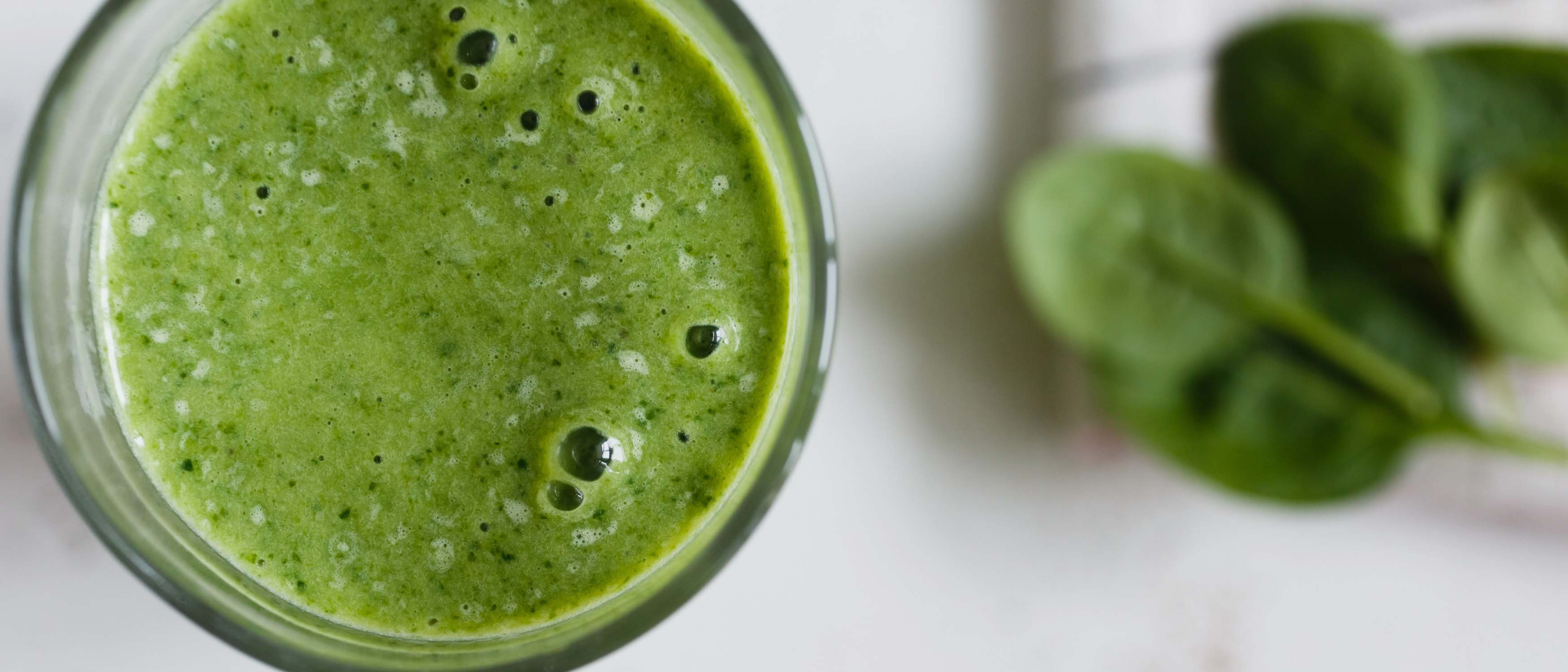 Fresh gut-friendly greens smoothie in a glass with baby spinach leaves